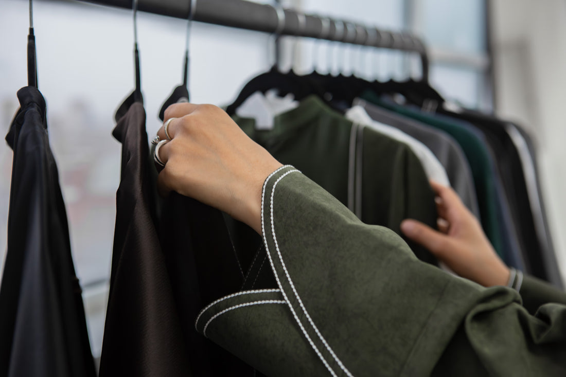 abayas hung up on a rain being adjusted by someone wearing a green abaya with embroidery detailing on it.